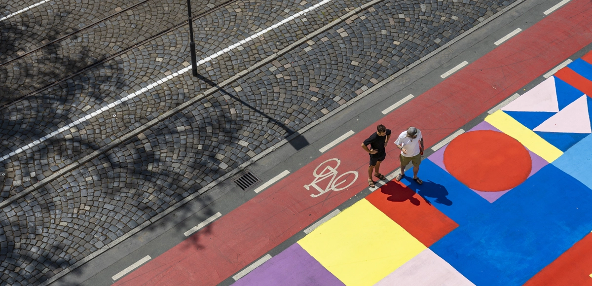 Urban Sports Park: Zwei Personen betrachten bemalte Bodenflächen mit geometrischen Formen in verschiedenen Farben.