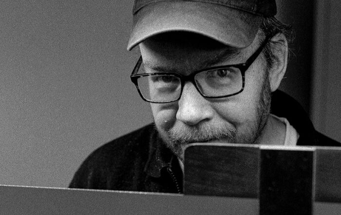 Schwarz-weiß Portrait von einem Mann mit Brille und Käppi. Er blickt selbstbewusst in die Kamera.