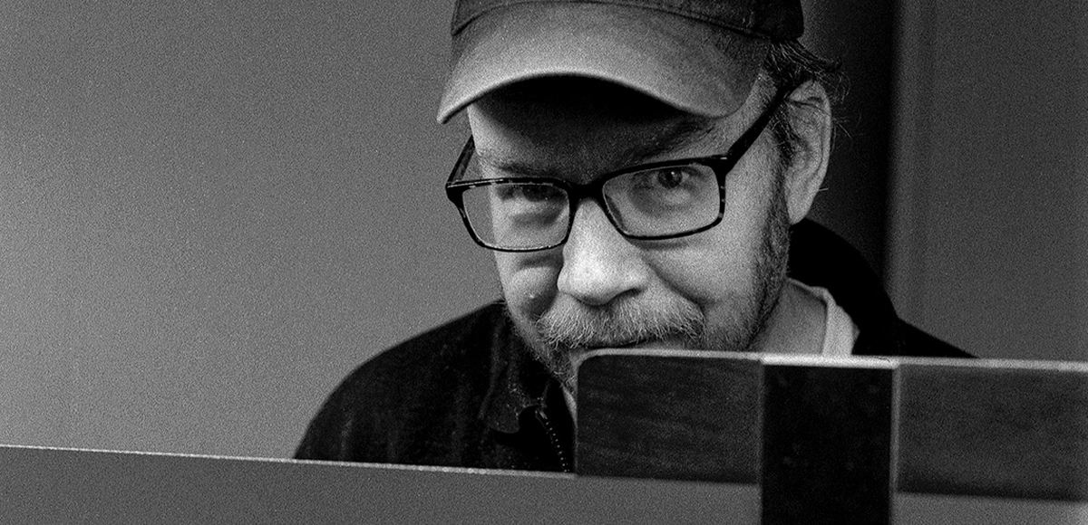 Schwarz-weiß Portrait von einem Mann mit Brille und Käppi. Er blickt selbstbewusst in die Kamera.