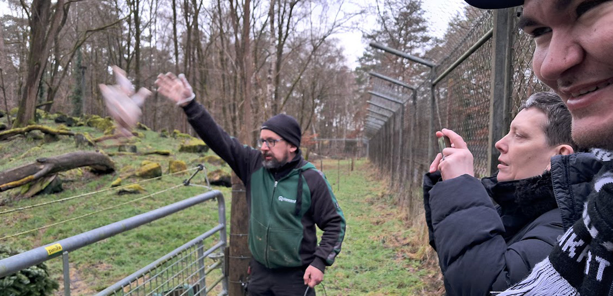 Zwei Personen schauen dem Tierpfleger beim Füttern der Tiere zu.