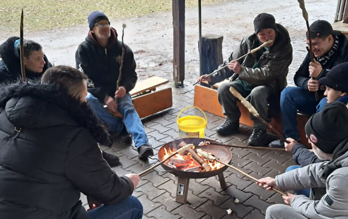 6 Personen am Lagerfeuer bereiten Stockbrot zu.