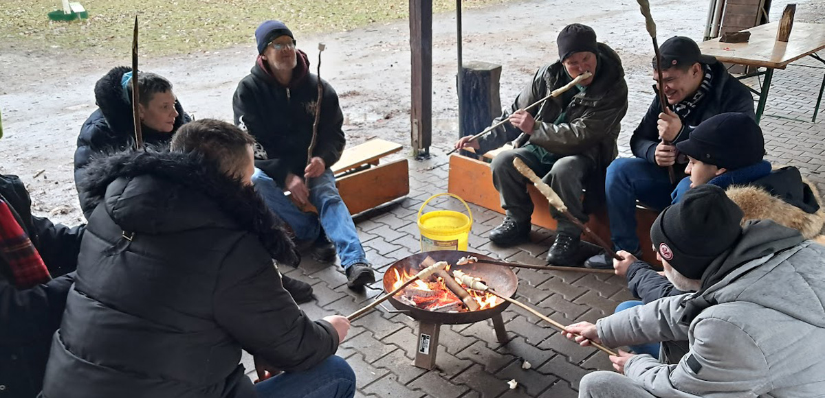 6 Personen am Lagerfeuer bereiten Stockbrot zu.