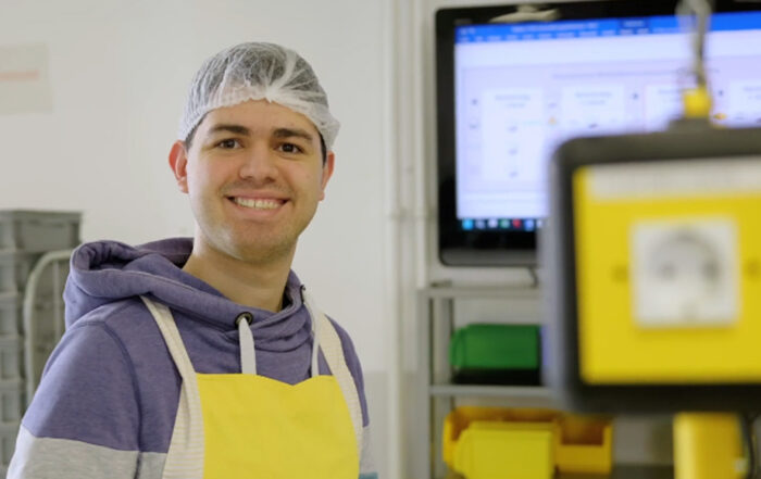 Mitarbeiter mit Schürze und Haarnetz lächelt in die Kamera.