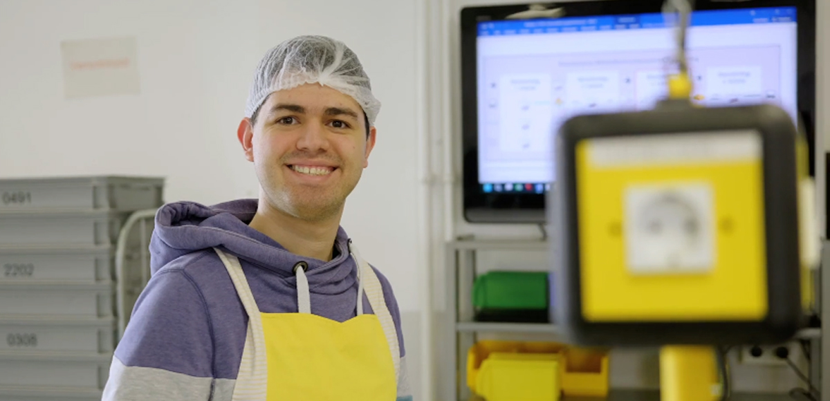 Mitarbeiter mit Schürze und Haarnetz lächelt in die Kamera.