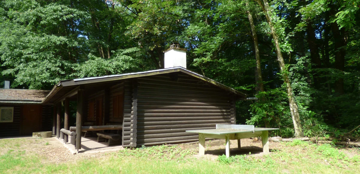 Holzhütte im Wald mit Tischtennisplatte davor.