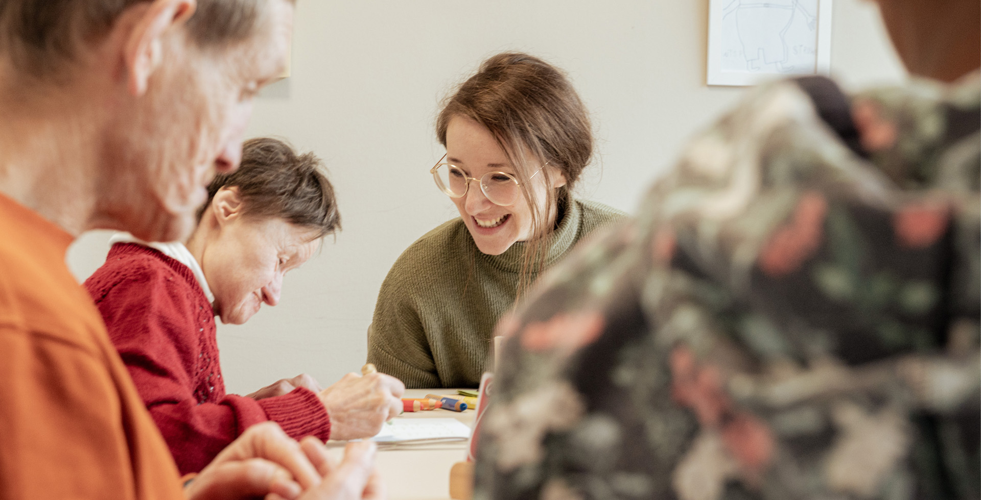 Menschen mit Behinderung sitzen an einem Tisch, eine Assistentin unterstützt.