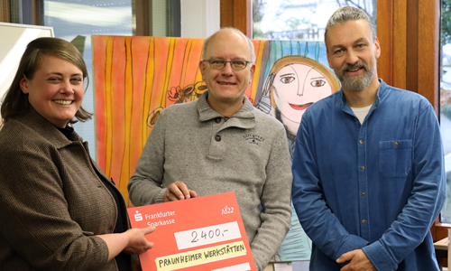 Werkstattleiterin nimmt einen Spenden-Scheck von zwei Männern entgegen.