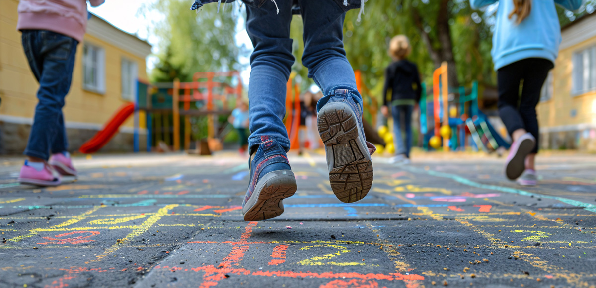Kinder spielen Hüpfkästchen auf dem Schulhof.